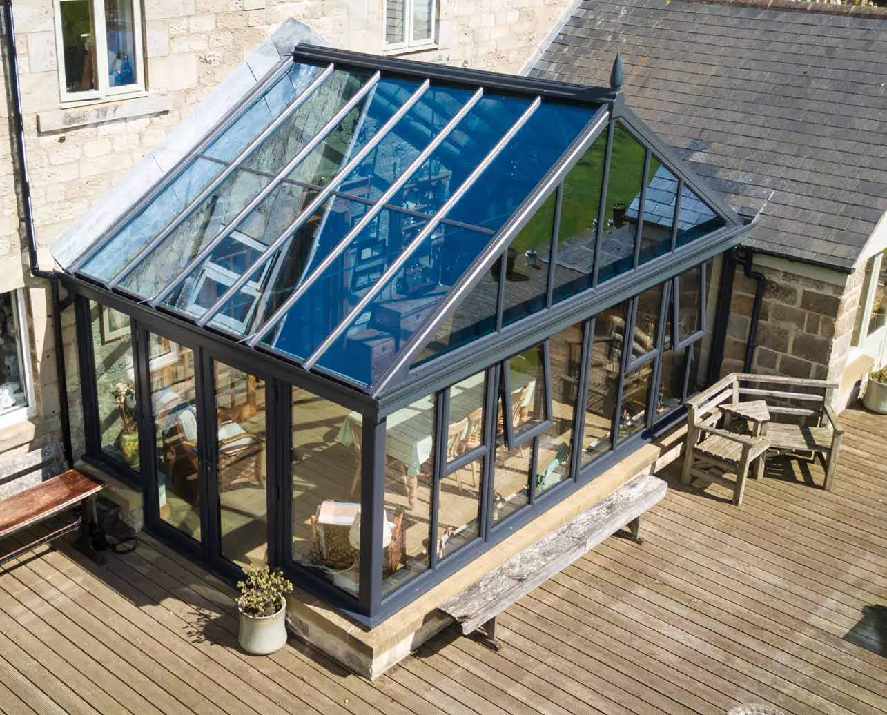 Aerial view of a dark-framed glazed conservatory beside a stone house