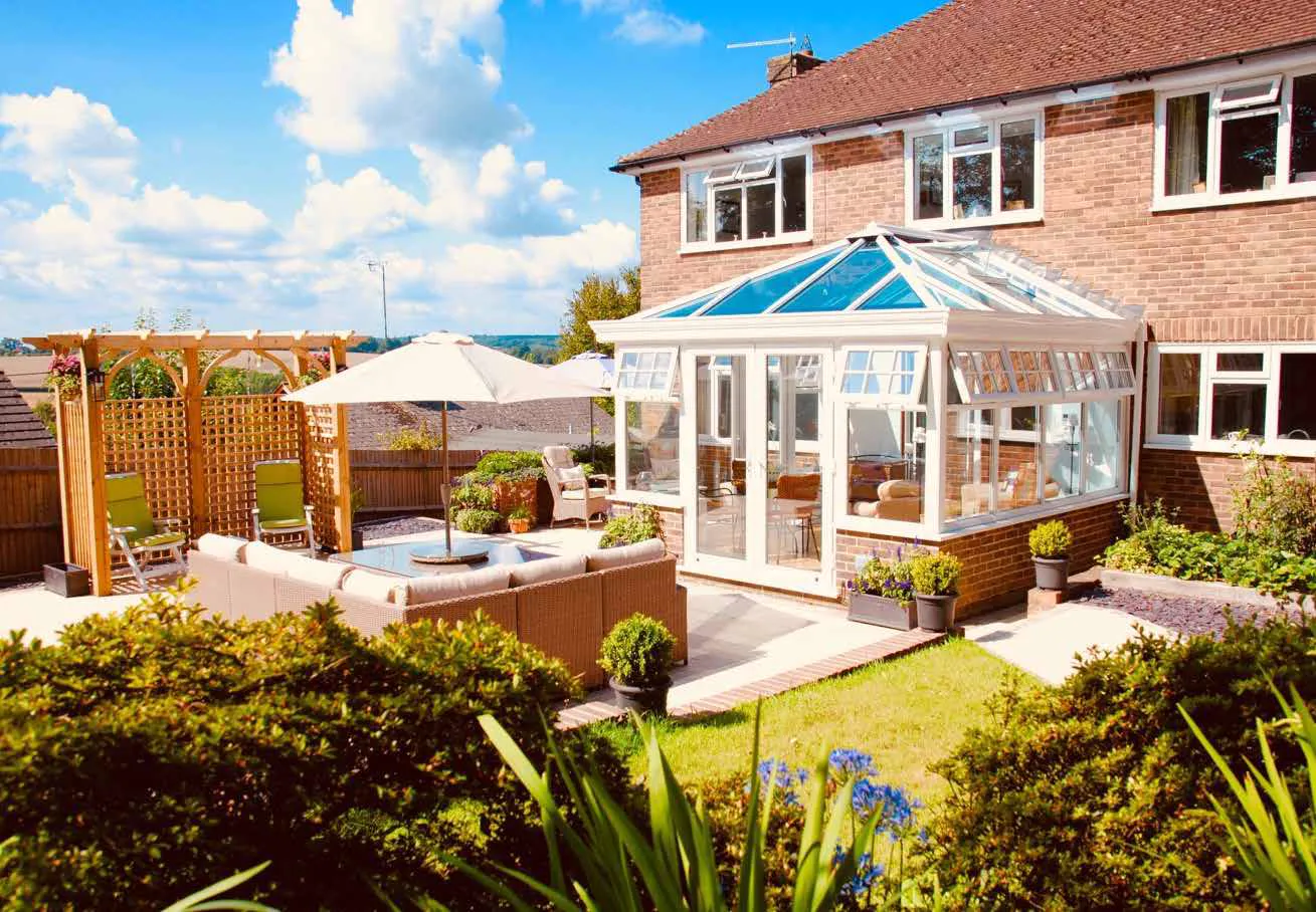 White-framed conservatory beside a sunny garden patio