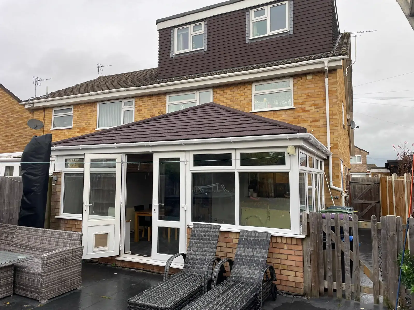 White-framed conservatory with a tiled roof and double doors beside garden decking