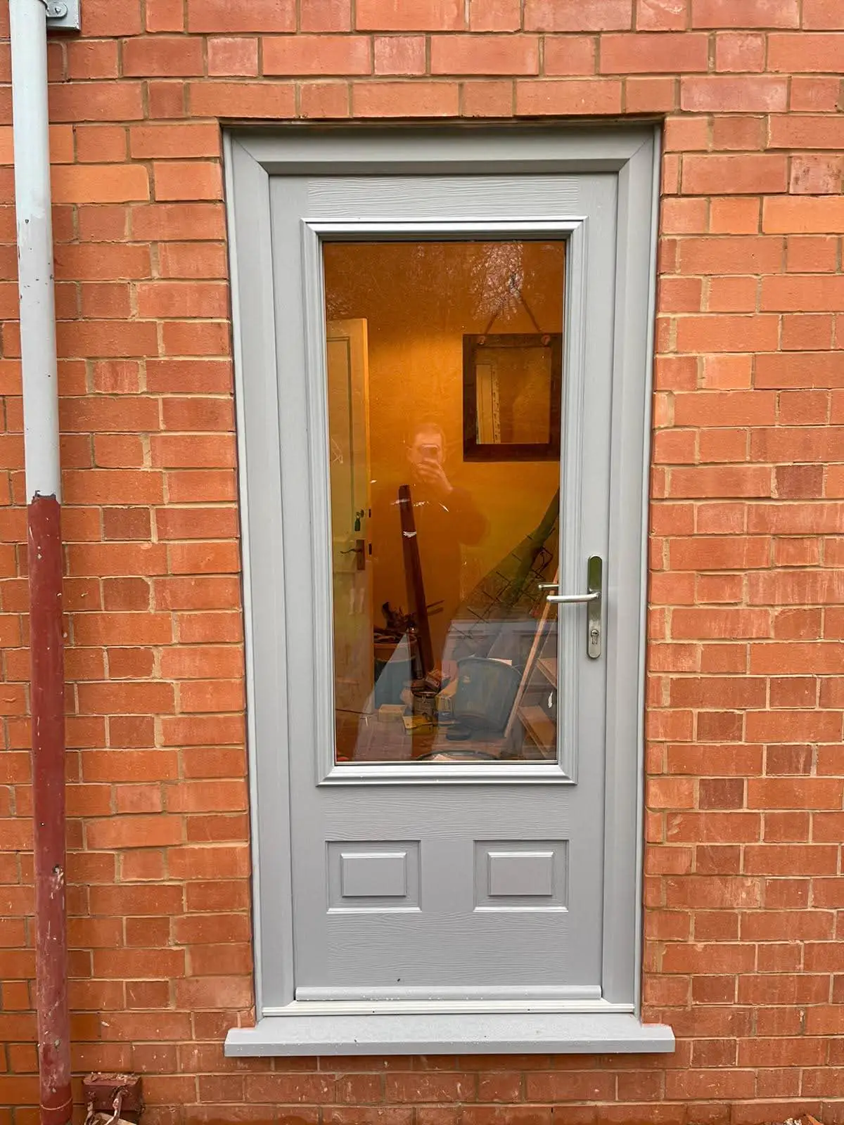 Grey entrance door with a tall glazed panel in a brick wall