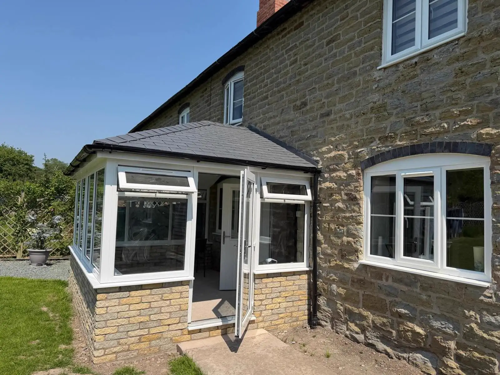 White-framed conservatory with a tiled roof adjoining a stone house