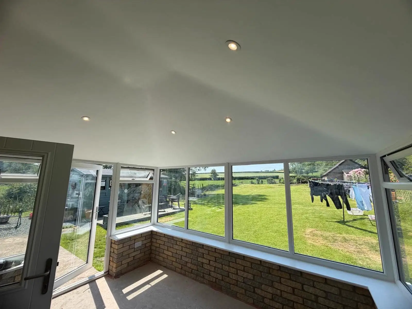 Conservatory interior with a vaulted white ceiling, recessed lights and a garden view