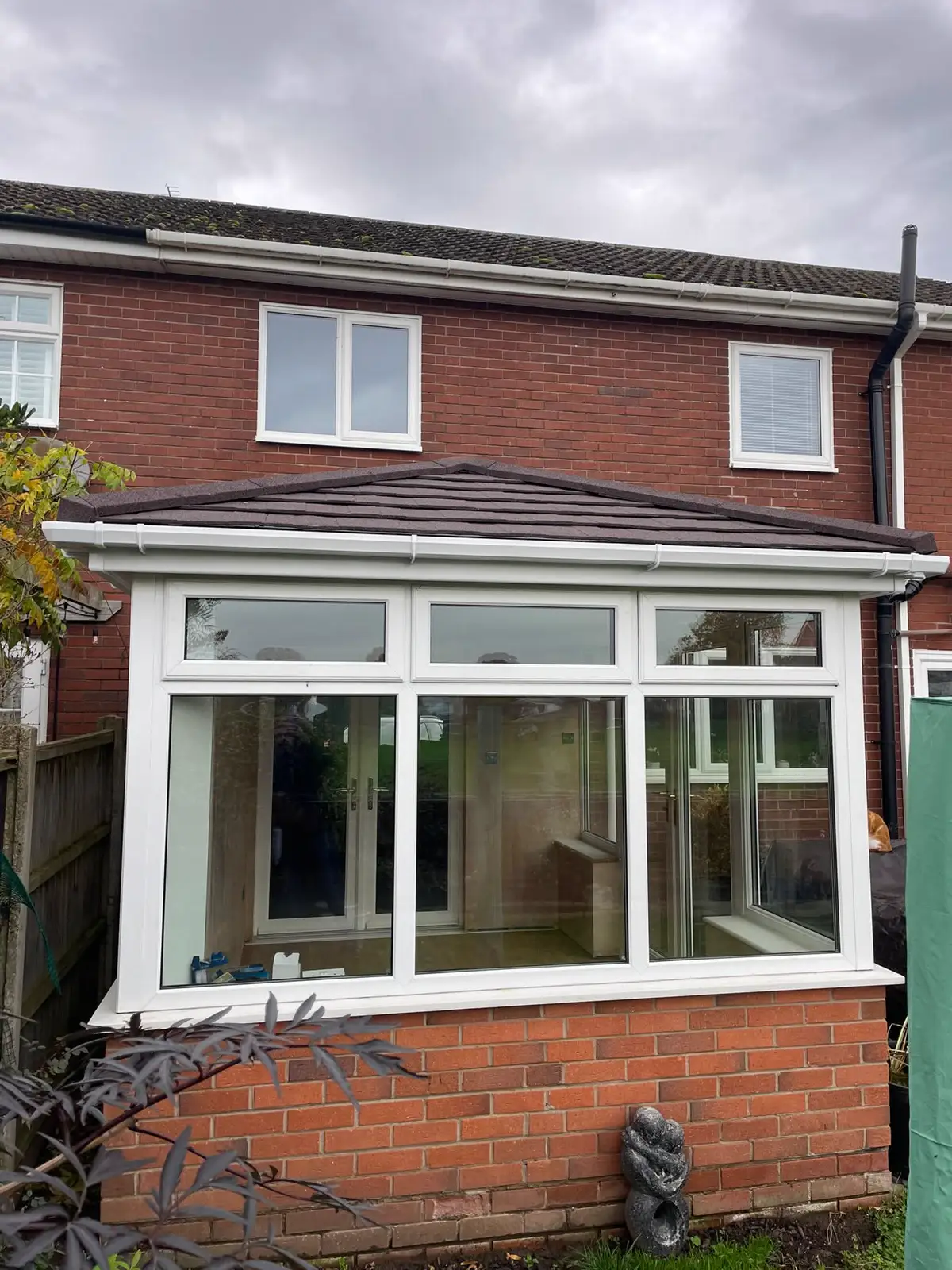 White-framed conservatory with a tiled roof, wide glazing and a brick base